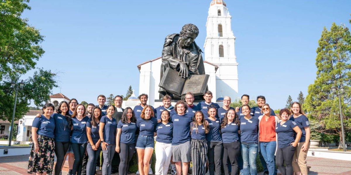 A group of Mission and Ministry workers posing in front of a chapel and a statue